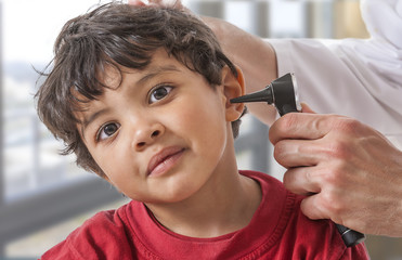 A pediatrician examining his boy patient's ear at doctor's office