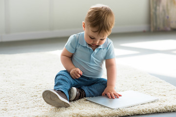 Fototapeta premium little baby boy with laptop sitting on floor at home