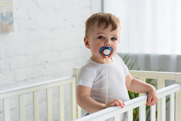 cute little baby boy with pacifier in baby crib looking at camera at home - obrazy, fototapety, plakaty