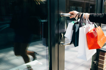 Female hand holding shopping bags and open door of shop