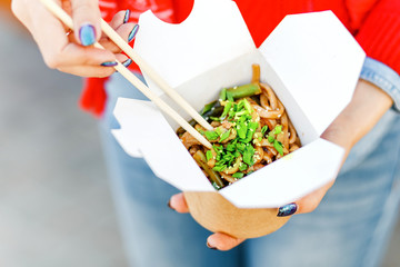Closeup macro view of a delicious Wok Noodles with greenery in takeout paper box with chop sticks