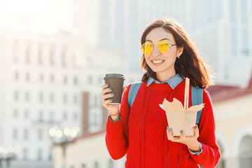 closeup of young asian woman with coffee cup and wok noodles paper box on city street