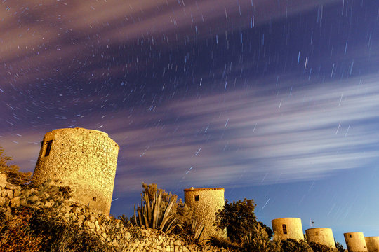 long exposure with towers or old mills with circumpolar stars and clouds on a mountain with vegetation