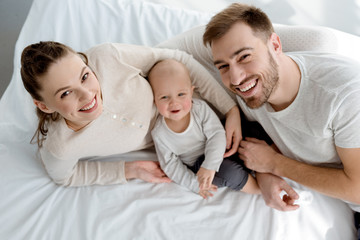 Fototapeta premium overhead view of happy young parents with infant lying on bed