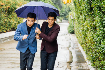 Gay couple holding umbrella and hands together. Asian homosexual men walking in the rain