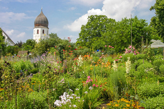 Idylle im Klostergarten des Klosters auf der Insel Frauenchiemsee, mit vielen bunten Blumen im Vordergrund und der Kirchturm im Hintergrund	