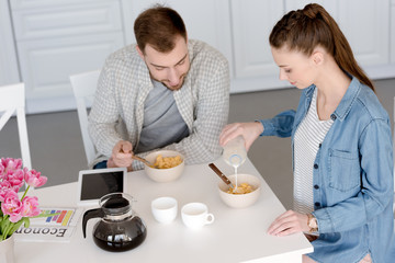 husband and wife having breakfast with corn flakes and coffee in kitchen with digital tablet