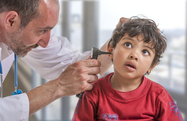 A pediatrician examining his boy patient's ear at doctor's office