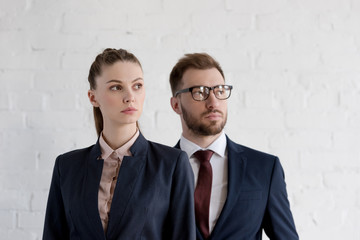confident businesspeople in formal wear posing near white wall