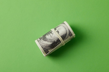 top view of roll of dollars tied with rubber band on green