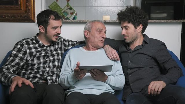 Old Father And his sons learns how to use Tablet Computer sitting on sofa 