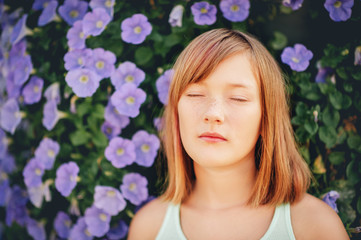 Daydreaming pretty kid girl, close up portrait against purple flower wall. Eyes closed