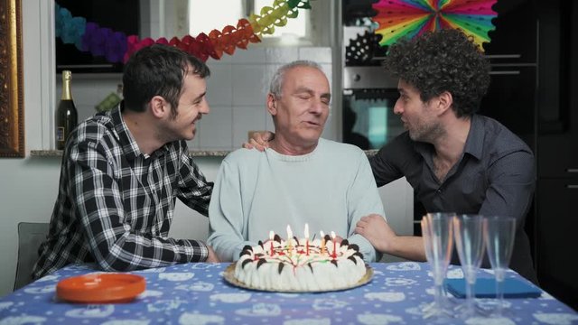 Old fatherblowing on the candles on his birthday cake with his sons