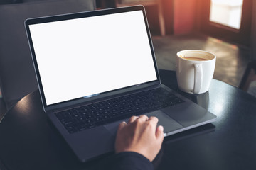 Mockup image of businessman using and typing on laptop with blank white screen and coffee cup on table in cafe