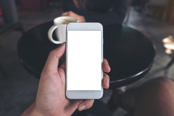 Mockup image of hand holding white mobile phone with blank screen in cafe and blur woman in background