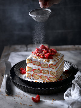 Close up of man dusting powdered sugar on berry and cream cake