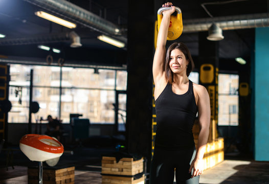 Fitness woman doing a weight training by lifting kettlebell. Muscular fitness woman, holds up a yellow kettlebell crossfit the gym. Fitness woman in the gym. Crossfit woman. Healthy lifestyle