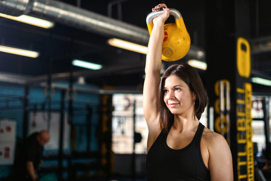 Fitness woman doing a weight training by lifting kettlebell. Muscular fitness woman, holds up a yellow kettlebell crossfit the gym. Fitness woman in the gym. Crossfit woman. Healthy lifestyle