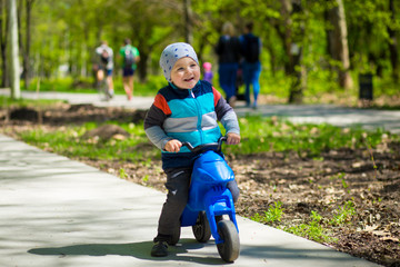 Obraz premium Little boy riding toy motorbike in green sunny park. Active childhood
