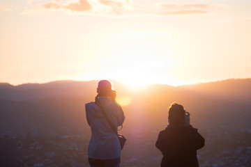 Two women taking a photo together at sunset over the mountain.