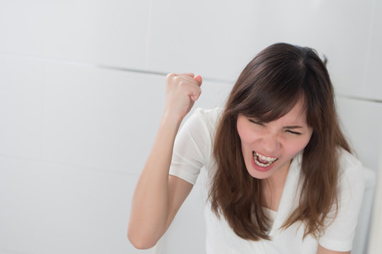 angry woman in toilet by diarrhea, constipation, hemorrhoids, piles; portrait of woman hard pushing in toilet or wc from diarrhea, constipation, food poisoning, hemorrhoids; asian adult woman model