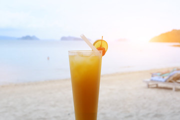 Fresh orange juice at the beach, Glass of orange juice on the sandy beach with sea in background