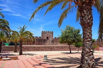 Fototapeta na wymiar Palm trees and landscaped gardens within the Medieval castle with battlements and tower to the rear, Silves, Portugal.