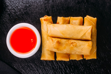 lumpias with sweet sauce on a black background