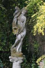 Fototapeta na wymiar Marmorfigur mit gelben Ginster im Garten