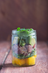 Hawaiian Poke salad with tuna, avocado and vegetables in a jar in the center on a rustic background