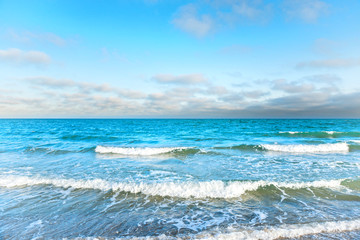 Fototapeta na wymiar Blue sea with waves, foam and white clouds on the sky