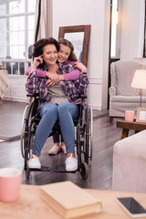 Best mom. Jolly girl embracing disabled woman who smiling