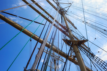 Masts of a sailing ship with the lowered sails with blue sky on the background.