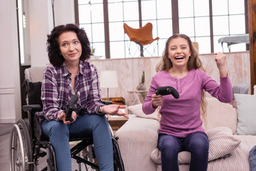 Game world. Jovial incapacitated woman and girl holding controller while gesturing