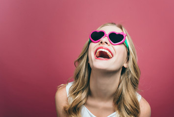A portrait of a girl that wars glasses. She is smiling and looking up. Girl is very cheerful. Isolated on pink background.
