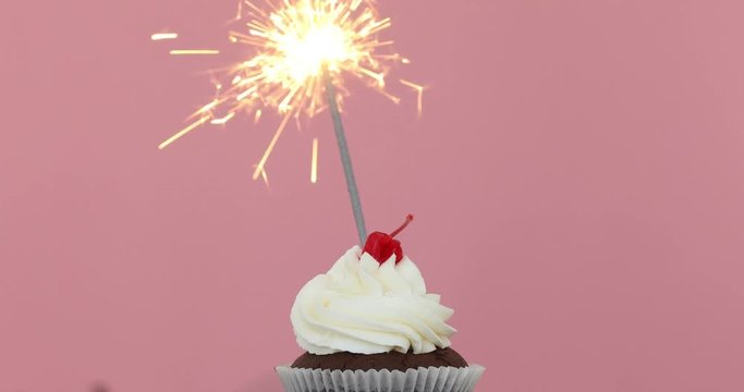 Birthday cupcake with a sparkler against a pink background