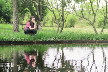 Woman fishing and relaxing, crouched in front of a lake, holding a bamboo fishing rod waiting patiently to catch a fish.