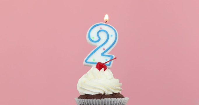 Number 2 candle in a cupcake against a pastel pink background blow out at the end