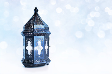 Ornamental dark Moroccan, Arabic lantern on the table. Burning candle, glittering bokeh lights...