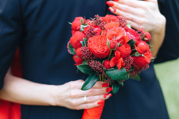 bride in a red dress with a red bouquet of a pion hugging her beloved