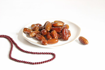 Closeup of porcelain plate with date fruits and prayer beads on the white table. Greeting card for...
