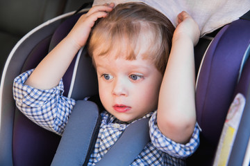 Portrait of the cute little boy who is sitting in the baby car seat in a car