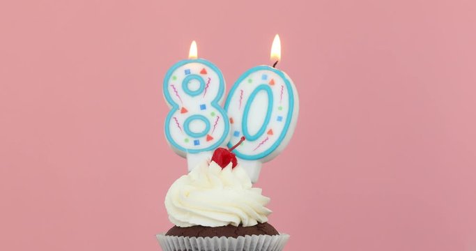 Number eighty 80 candle in a cupcake against a pastel pink background blow out at the end