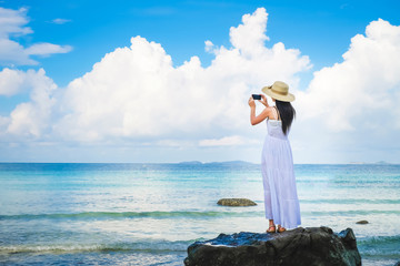 woman traveler enjoying for view of the beautiful sea on her holiday. Lady tourist standing and taking photo on the beach.