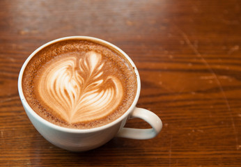 Latte coffee in white cup lay on wooden table