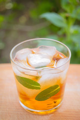 cold tea with ice and mint in a glass on a wooden background in the garden