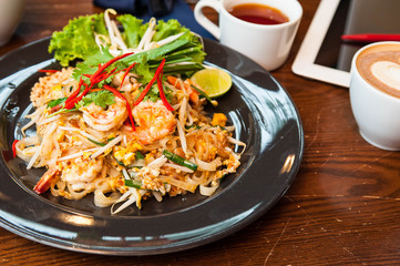 Pad Thai with Shrimp in black plate on wooden table,Look tasty Thai food,coffee and tea with Padthai lay on wooden table,Thai food for meal time