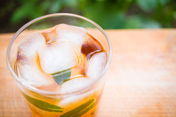 cold tea with ice and mint in a glass on a wooden background in the garden
