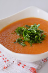 Cream soup of baked pepper in a white plate decorated with parsley leaves.