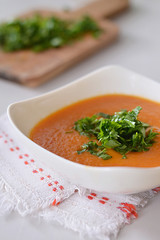 Soup puree of baked pepper in a white plate decorated with parsley leaves.